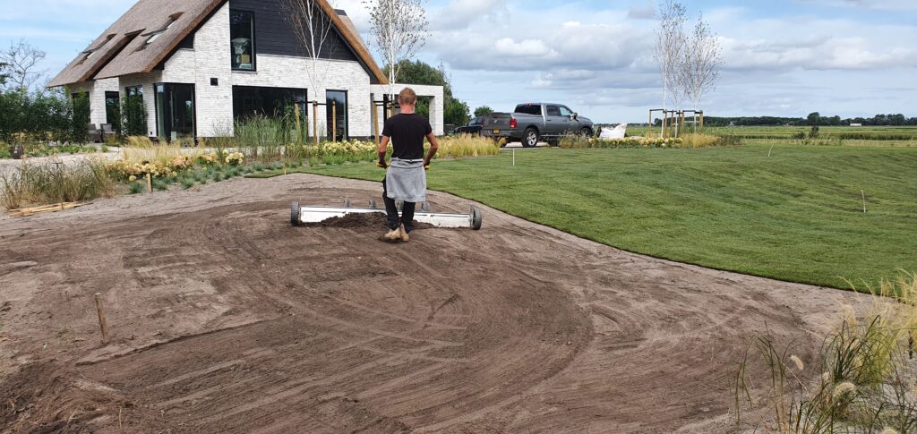Hovenier van De Gaarde Hoveniers werkt aan het aanleggen van een tuin, met behulp van moderne tuingereedschappen.