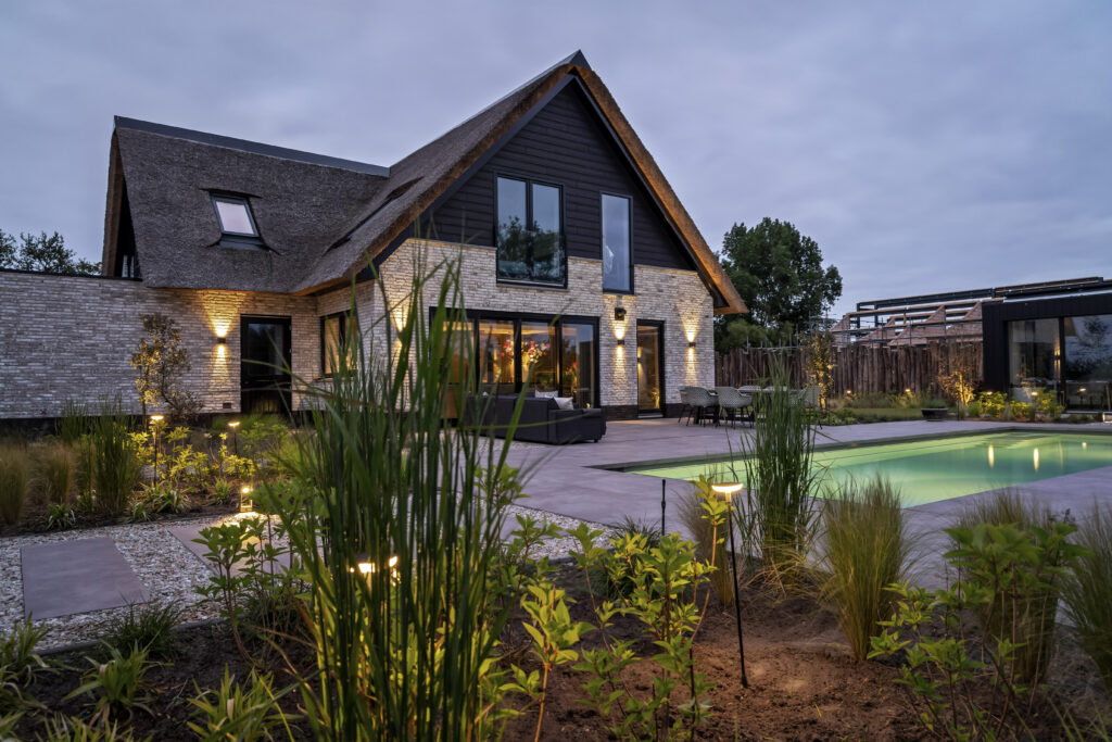 Een tuin met sfeervolle verlichting en zwembad, gecreëerd door De Gaarde Hoveniers voor een luxueuze uitstraling.